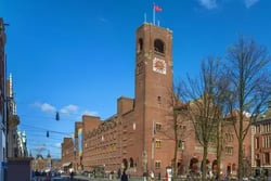 Beurs van Berlage in Amsterdam aan het Damrak: historisch bakstenen beursgebouw met hoge toren en klok, gezien vanaf de straat op een zonnige dag met blauwe lucht en bomen. Hier vindt Emerce E-commerce Live! plaats.