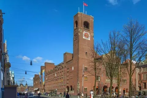 Beurs van Berlage in Amsterdam aan het Damrak: historisch bakstenen beursgebouw met hoge toren en klok, gezien vanaf de straat op een zonnige dag met blauwe lucht en bomen. Hier vindt Emerce E-commerce Live! plaats.