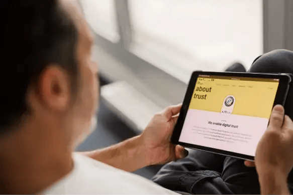 Persoon bekijkt Trusted Shops-website op een tablet. Op het scherm de ‘About trust’-pagina met Trusted Shops-keurmerk en uitleg over digitale betrouwbaarheid. Beeld illustreert online vertrouwen, keurmerken en e‑commerce security.