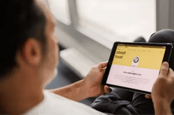 Persoon bekijkt Trusted Shops-website op een tablet. Op het scherm de ‘About trust’-pagina met Trusted Shops-keurmerk en uitleg over digitale betrouwbaarheid. Beeld illustreert online vertrouwen, keurmerken en e‑commerce security.