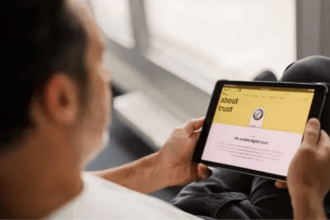Persoon bekijkt Trusted Shops-website op een tablet. Op het scherm de ‘About trust’-pagina met Trusted Shops-keurmerk en uitleg over digitale betrouwbaarheid. Beeld illustreert online vertrouwen, keurmerken en e‑commerce security.