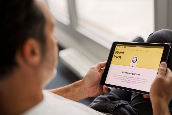 Een man kijkt op een tablet. Daarop zie je een pagina met 'About trust' en 'We enable digital trust'