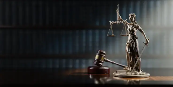 Afbeelding van een beeldje van Vrouwe Justitia, naast een hamer in een rechtszaal