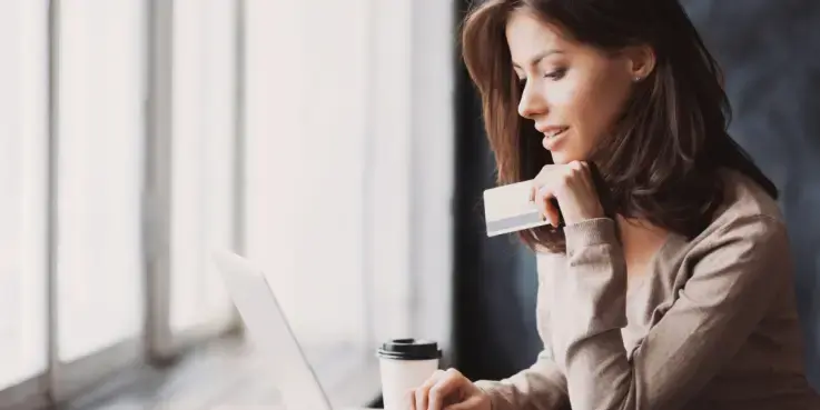 Een vrouw heeft een creditcard in de hand en kijkt naar haar laptop, ze kiest haar betaalmethode