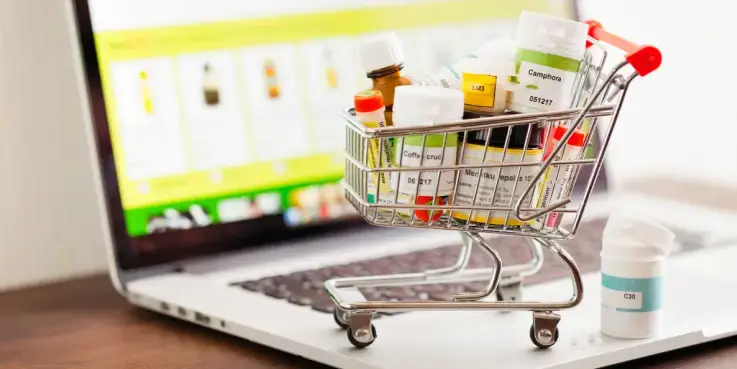 Miniwinkelwagentje gevuld met medicijnen staat op een laptop met een online apotheekwebsite op het scherm, symbool voor het bestellen van geneesmiddelen via internet en de groei van online apotheken.