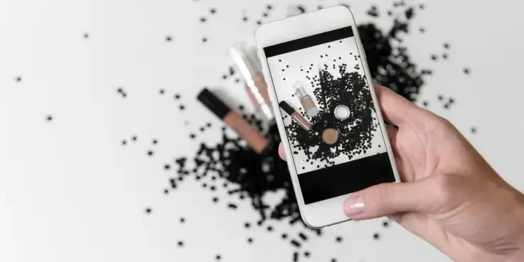 Hand die met een smartphone een foto maakt van make‑up producten op een ondergrond met zwarte korrels; voorbeeld van visuele content voor effectieve Instagram‑advertenties.