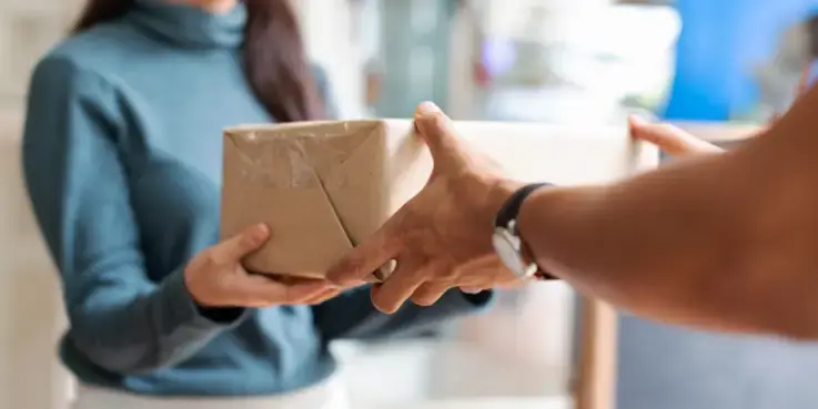 Foto van twee personen, beide onscherp. Het lijkt op een vrouw in een blauw shirt die een pakket aanneemt.