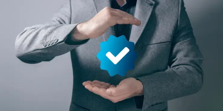 Man in grijs pak die een digitaal blauw verificatievinkje vasthoudt, symbool voor geverifieerde accounts op social media.