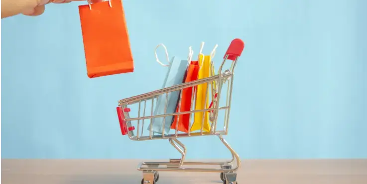 Afbeelding van een winkelkarretje met 3 winkeltassen erin. Een grote hand zet nog een winkeltas erin. Is een minimum orderwaarde slim?